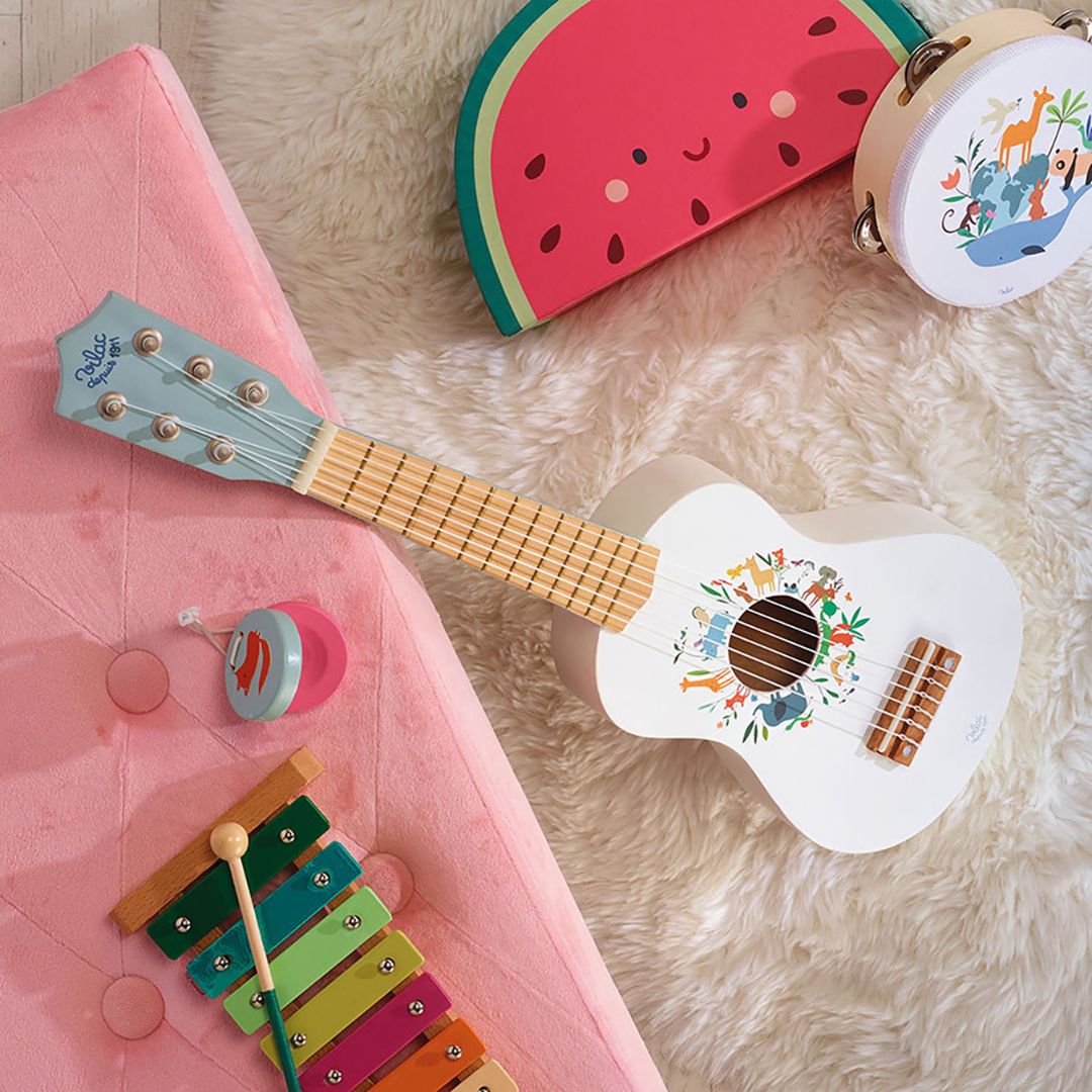 Hvid legetøjsguitar set i værelse med legetøj. Smuk guitar i træ til børn fra Vilac fås hos Nordic Simply