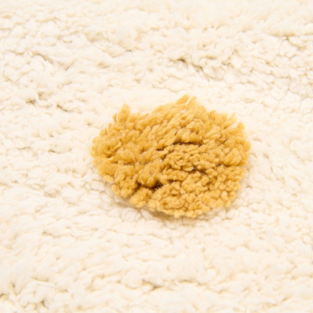 Gulvtæppe lyst med prikker, økologisk bomuld, set tæt på med blød plet i okkergul farve.