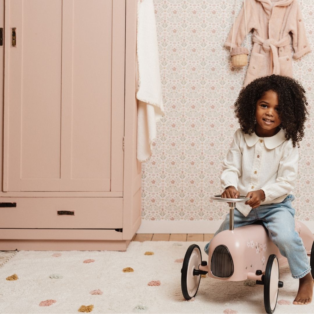 Aflangt gulvtæppe i beige med fine prikker, lavet i økologisk bomuld, kan maskin-vaskes, set med barn på legetøjsbil i hyggeligt rosa værelse.