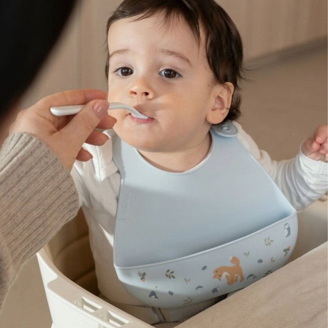 baby, med blå hagesmæk med opsamlingslomme og sødt motiv af ræv, får mad.