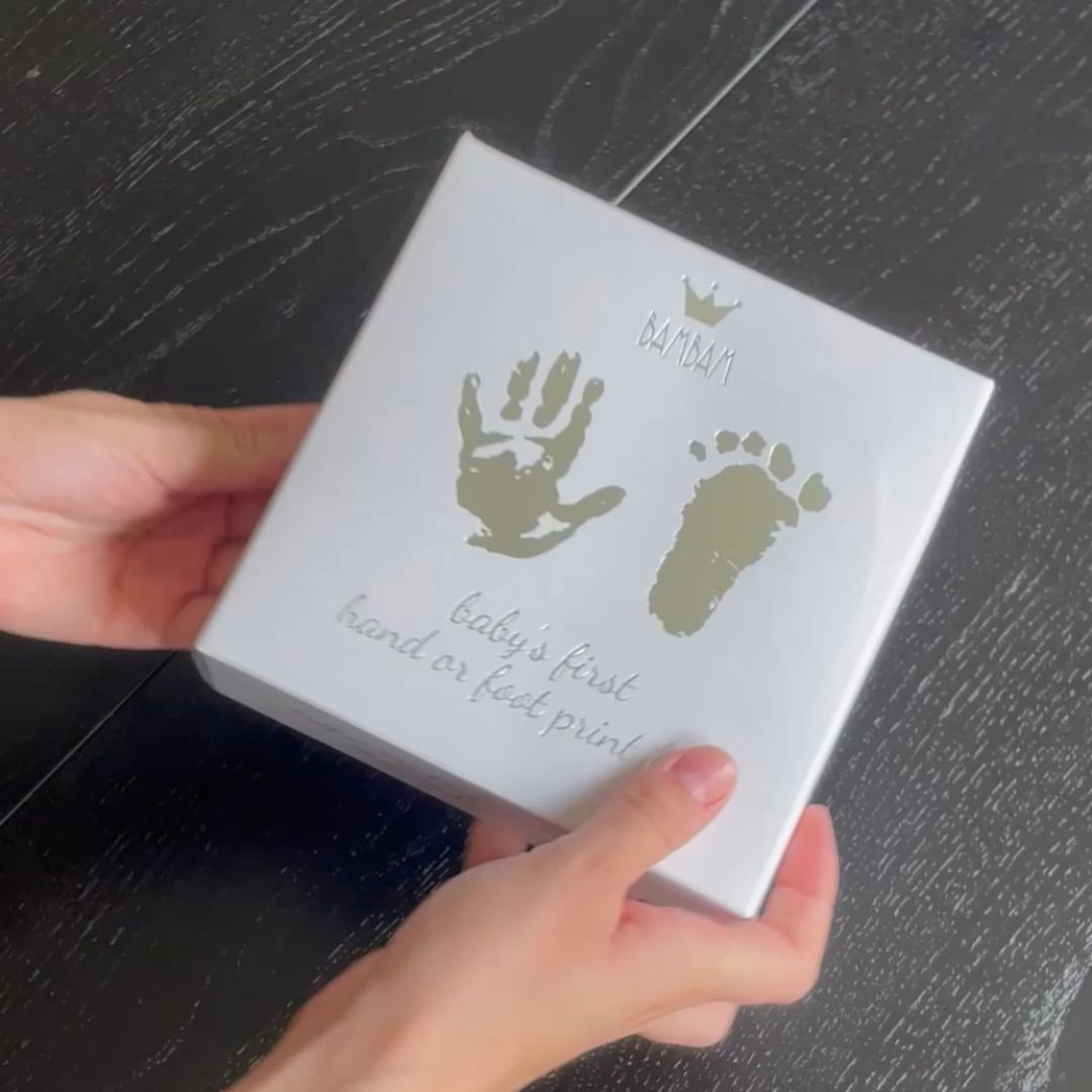 Hænder holder hvid gaveæske med sæt til at lave babys første hånd og fodaftryk i gips fra BamBam fås hos Nordic Simply