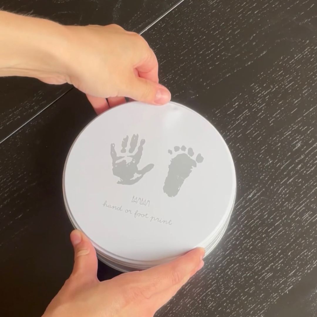 hænder åbner rund hvid dåse med sæt til at lave babys første hånd og fodaftryk i gips fra BamBam fås hos Nordic Simply