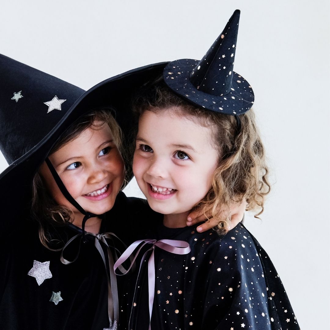 To piger i sort udklædning som hekse, pige til højre bærer lille heksehat på hårbøjle i sort velour med stjerner, fra Mimi & Lula fås hos Nordic Simply