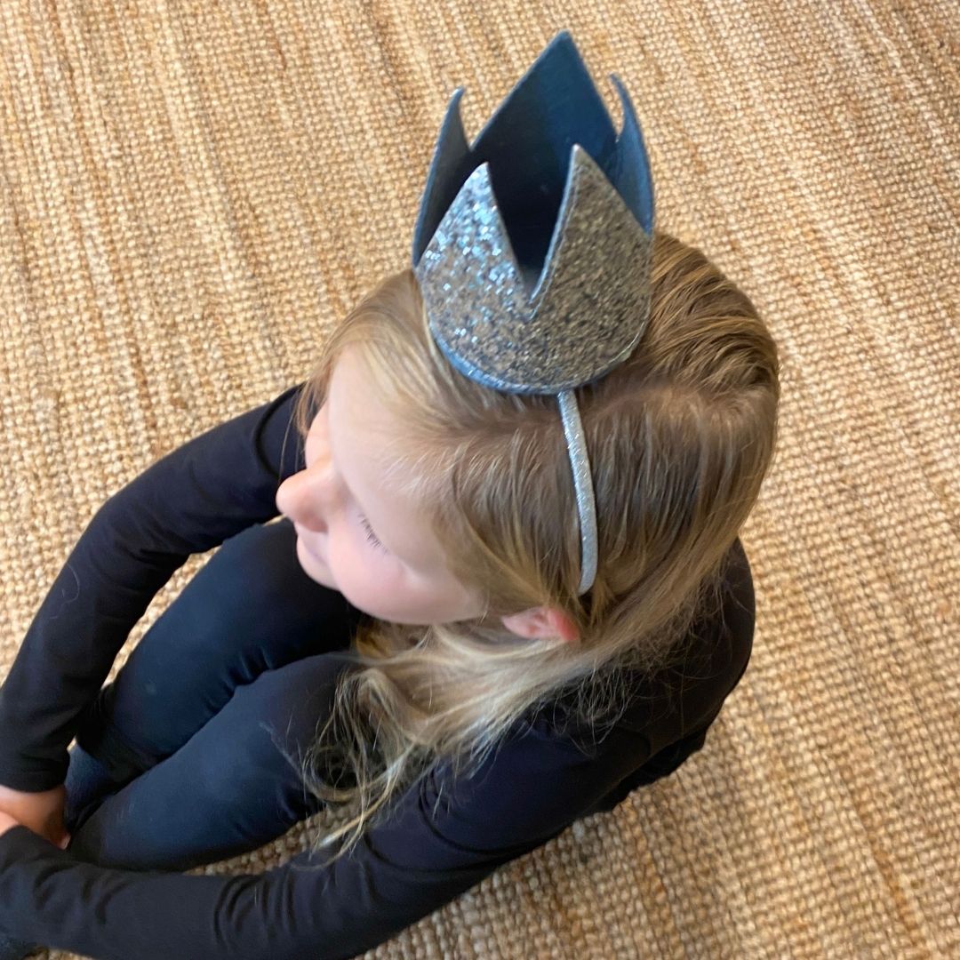 Pige sidder, set oppefra, med hårbøjle med sølvkrone i stof, perfekt til udklædning eller fest for børn fra 3 til 8 år fra Mimi & Lula fås hos Nordic Simply