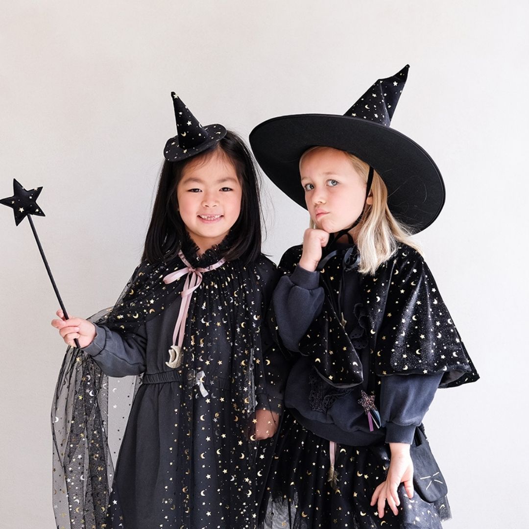 To piger i sort udklædning som hekse, pige til højre bærer høj sort heksehat i velour med guldstjerner og måner, fra Mimi & Lula fås hos Nordic Simply