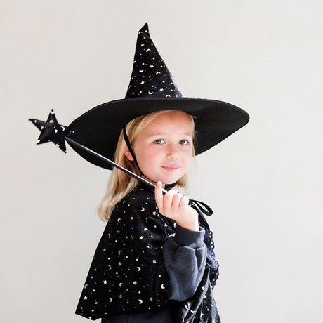 Pige med sort tryllestav, kappe og høj sort heksehat i velour med guldstjerner og måner, fra Mimi & Lula fås hos Nordic Simply