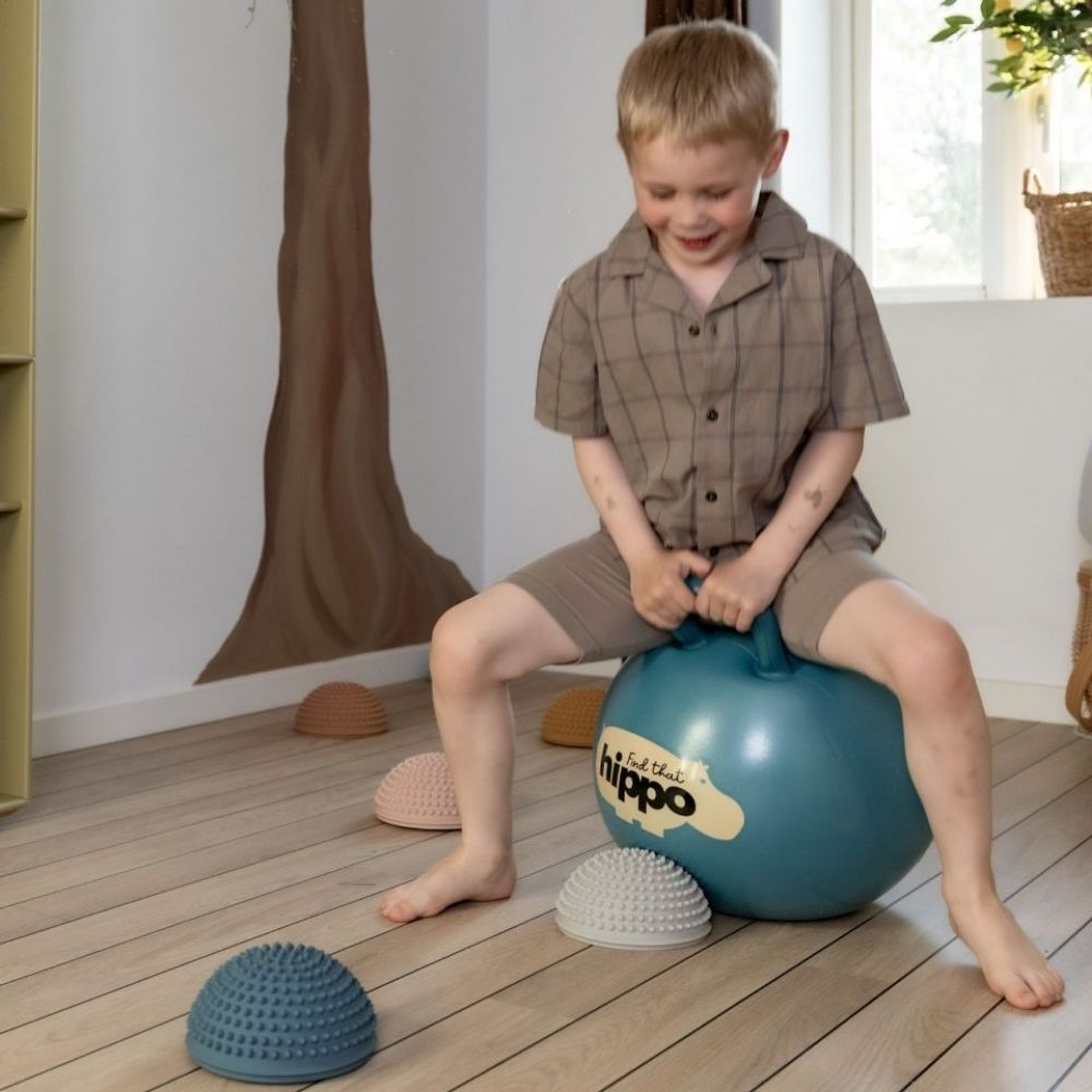 Barn i stue leger på blå hoppebold med håndtag fra Find that Hippo.