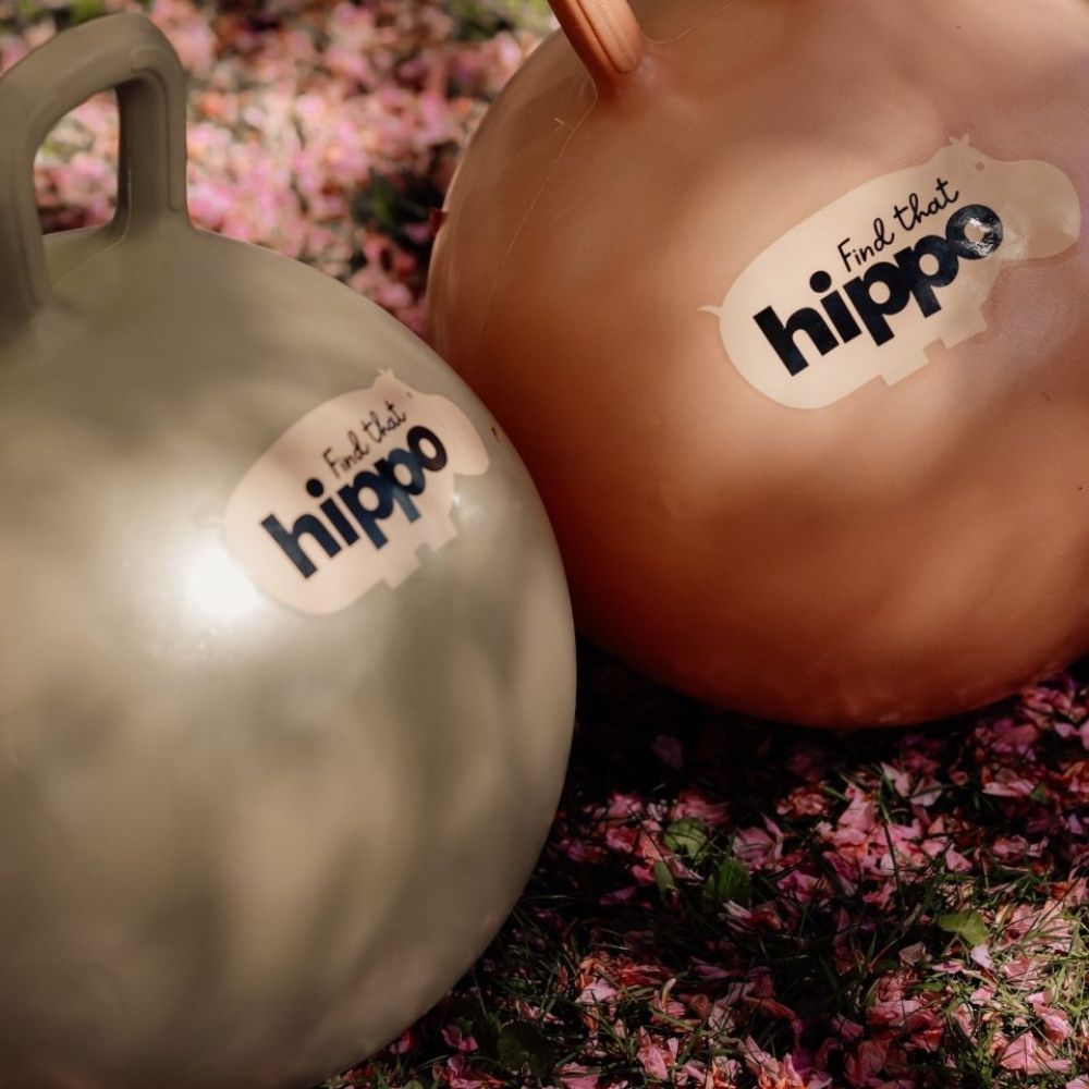 Grøn og orange hoppebold med håndtag ligger i skovbund med rosa blomster, til børn fra 2 år fra Find that Hippo fås hos Nordic Simply
