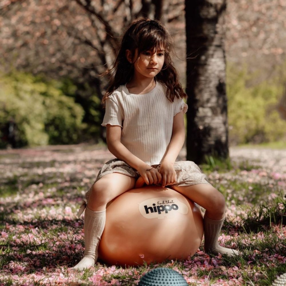 Pige leger i en park på orange hoppebold fra Find that Hippo til sjov, aktiv leg og motorisk træning, fås hos Nordic Simply