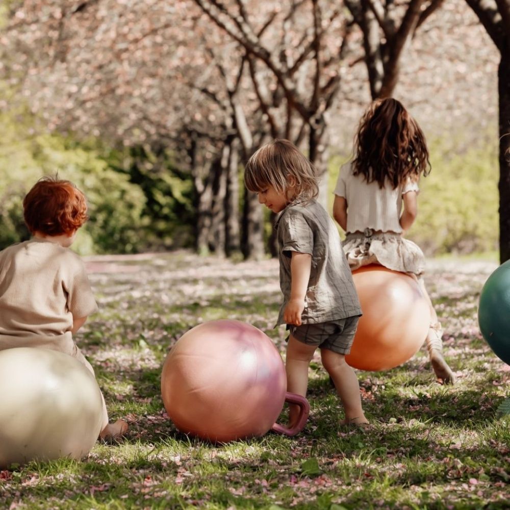 Børn leger i en park med rosa, orange og blå hoppebolde fra Find that Hippo til sjov, aktiv leg og motorisk træning, fås hos Nordic Simply
