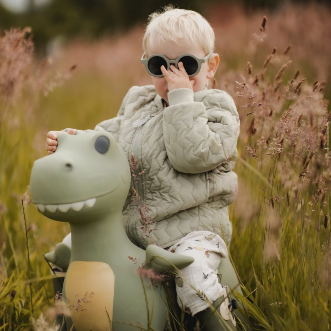 barn sidder på støvet grøn dino hoppedyr i seng med termotøj og solbriller på, dino hoppedyret Dexter er fra Find that Hippo og fås hos Nordic Simply