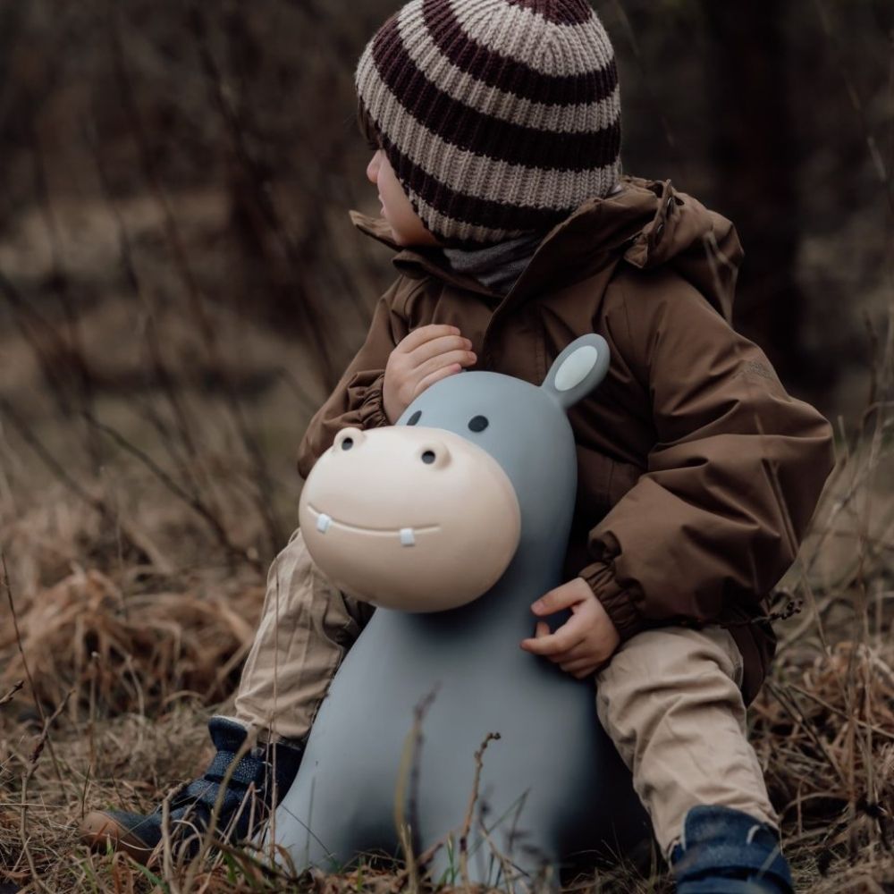 Barn sidder på et flodhest hoppedyr i lys grå, perfekt til leg og motoriktræning i naturen.
