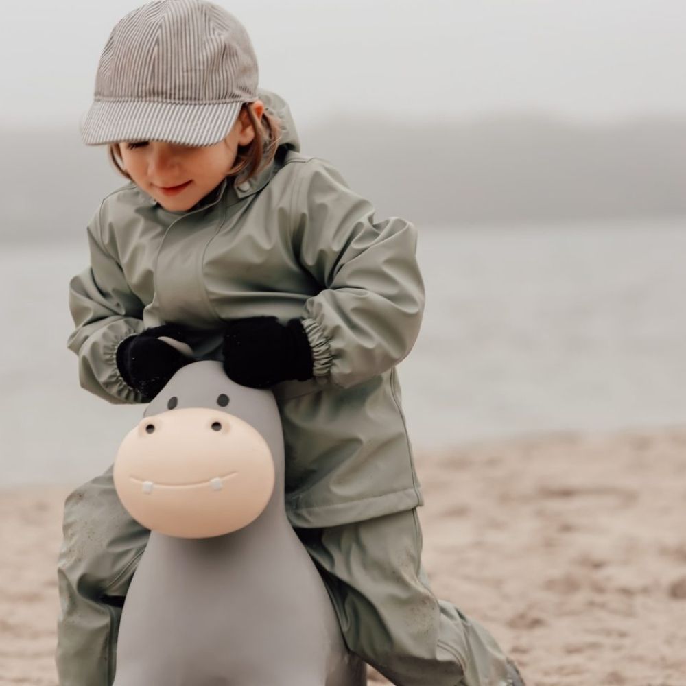 Barn der rider på lys grå flodhest hoppedyr, iført regnsæt, perfekt til leg og balanceøvelser.