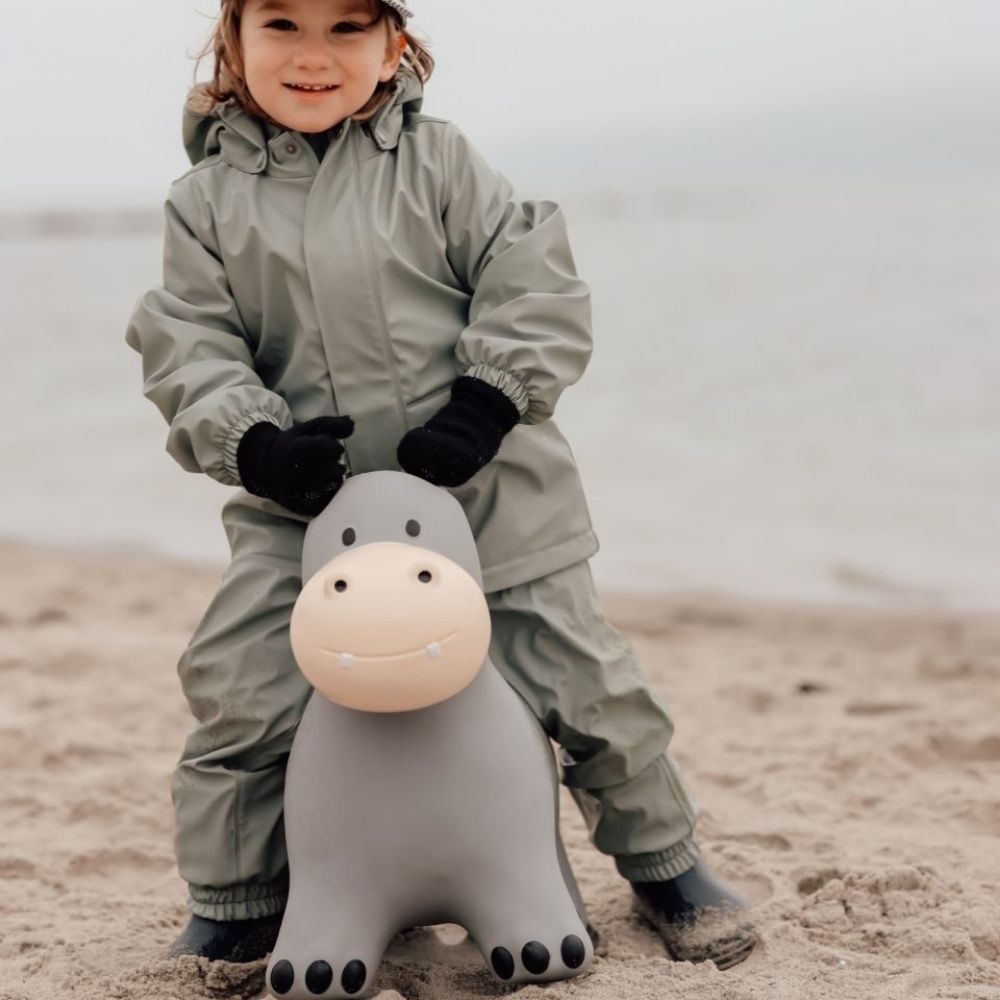 Barn leger på flodhest hoppedyr i lys grå, der træner balance og motorik ved stranden.
