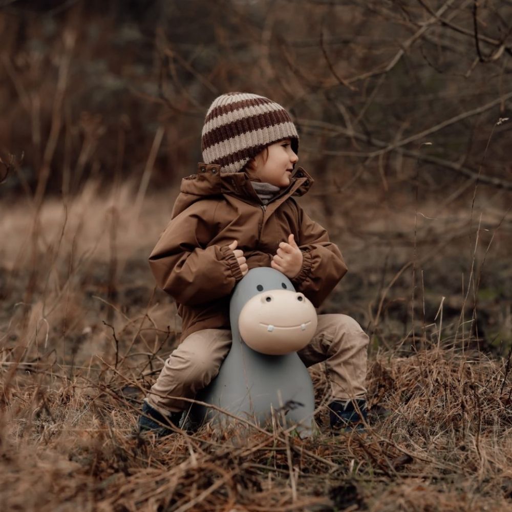 Barn i brunt overtøj leger på lys grå flodhest hoppedyr i naturen, fremmer balance og koordination.
