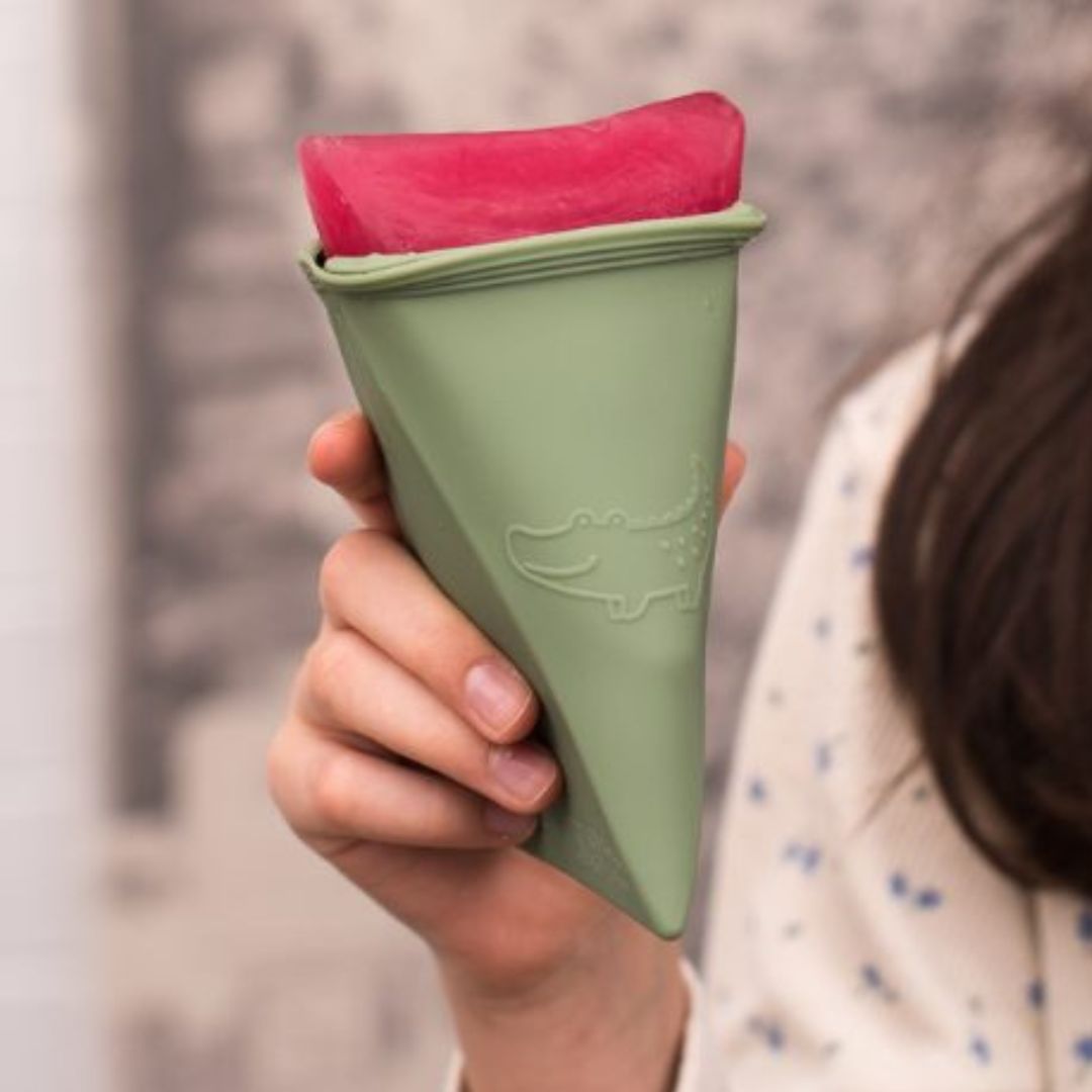 Hånd holder trekantet grøn isform med rød is, trekant isforme til at lave is fra We Might Be Tiny, fås hos Nordic Simply