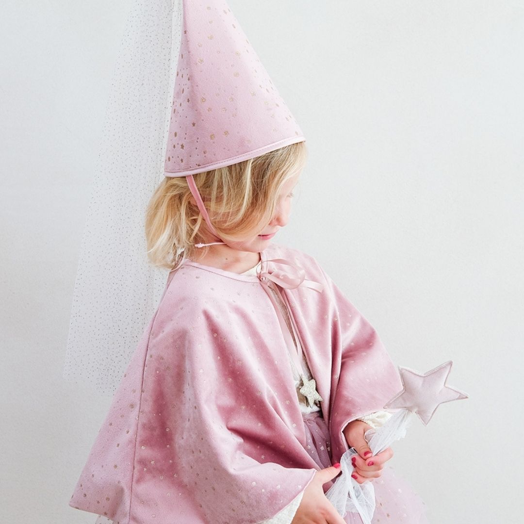 Pige set fra siden med høj rosa hat, rosa tryllestav og kort rosa kappe i velour med små guldstjerner, bindebånd i rosa satin og knaplukning, smuk udklædning i høj kvalitet til børn fra 3 år og op fra Mimi & Lula fås hos Nordic Simply