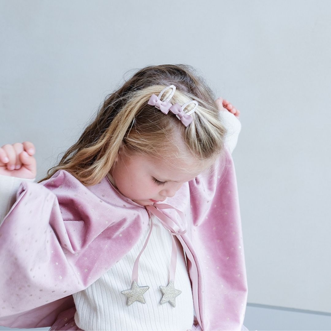 Pige set fra siden med rosa kappe i velour dekoreret med små guldstjerner, bindebånd i rosa satin med guldstjerner og knaplukning, smuk udklædning i høj kvalitet til børn fra 3 år og op fra Mimi & Lula fås hos Nordic Simply