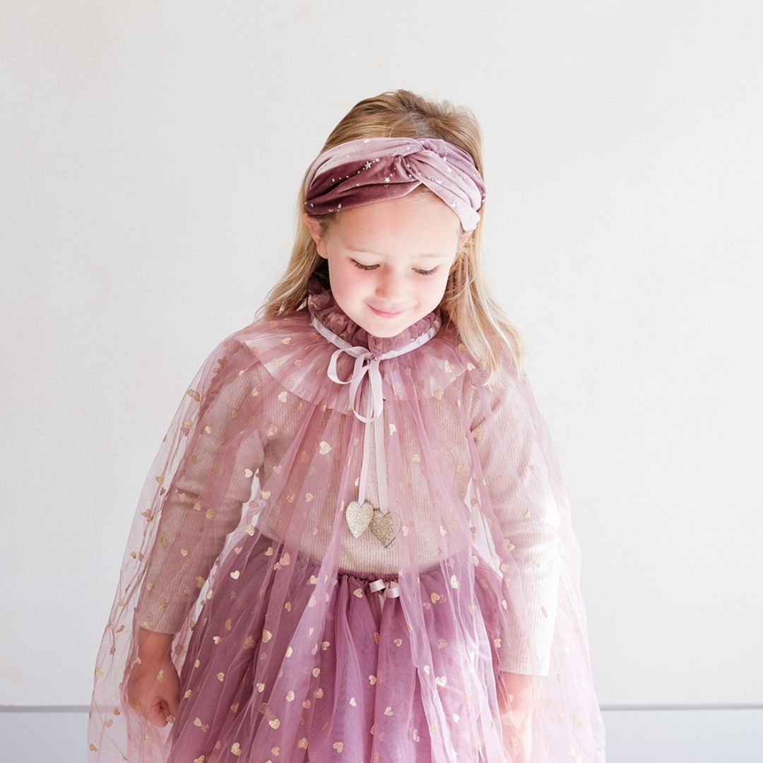 Pige i lang rosa kappe i tyl med bindebånd i satin, knaplukning og små guldstjerner, smuk udklædning i høj kvalitet, fra Mimi & Lula fås hos Nordic Simply