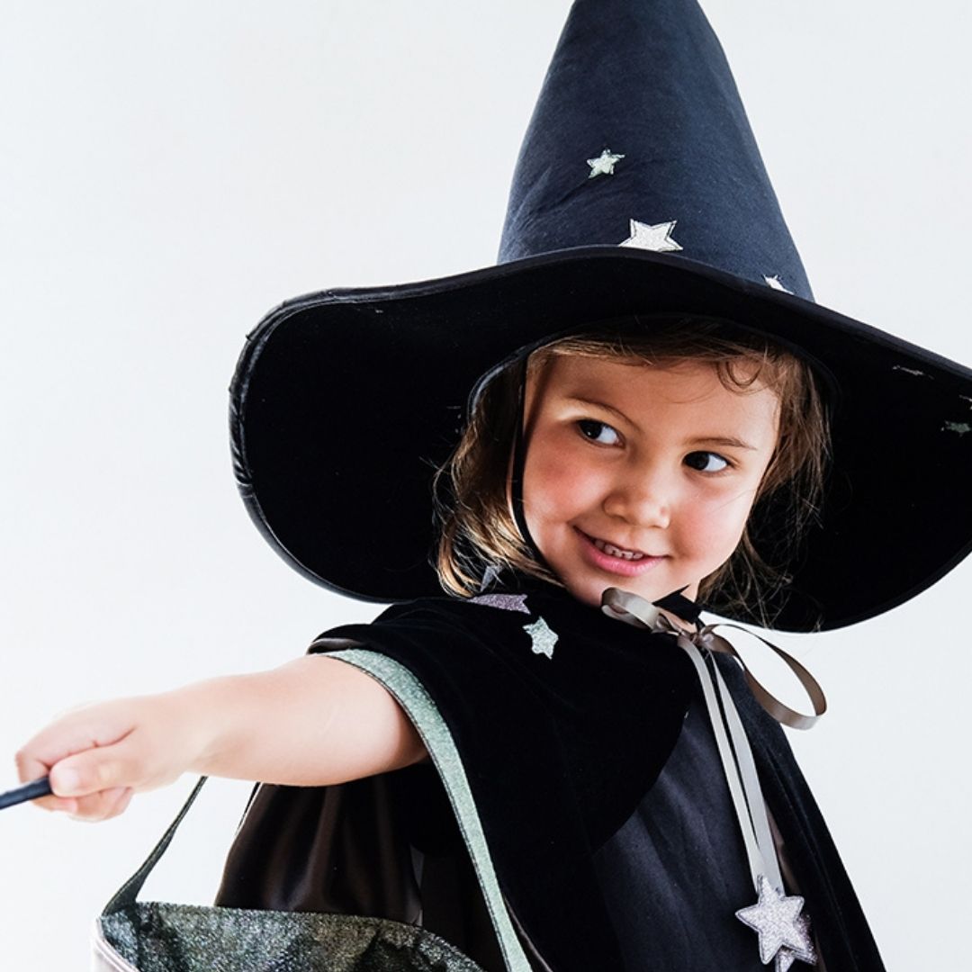 Pige med sort heksehat og sort kappe i velour med satinbindebånd og sølvstjerner, flot udklædning til børn fra 3 år og op fra Mimi & Lula fås hos Nordic Simply