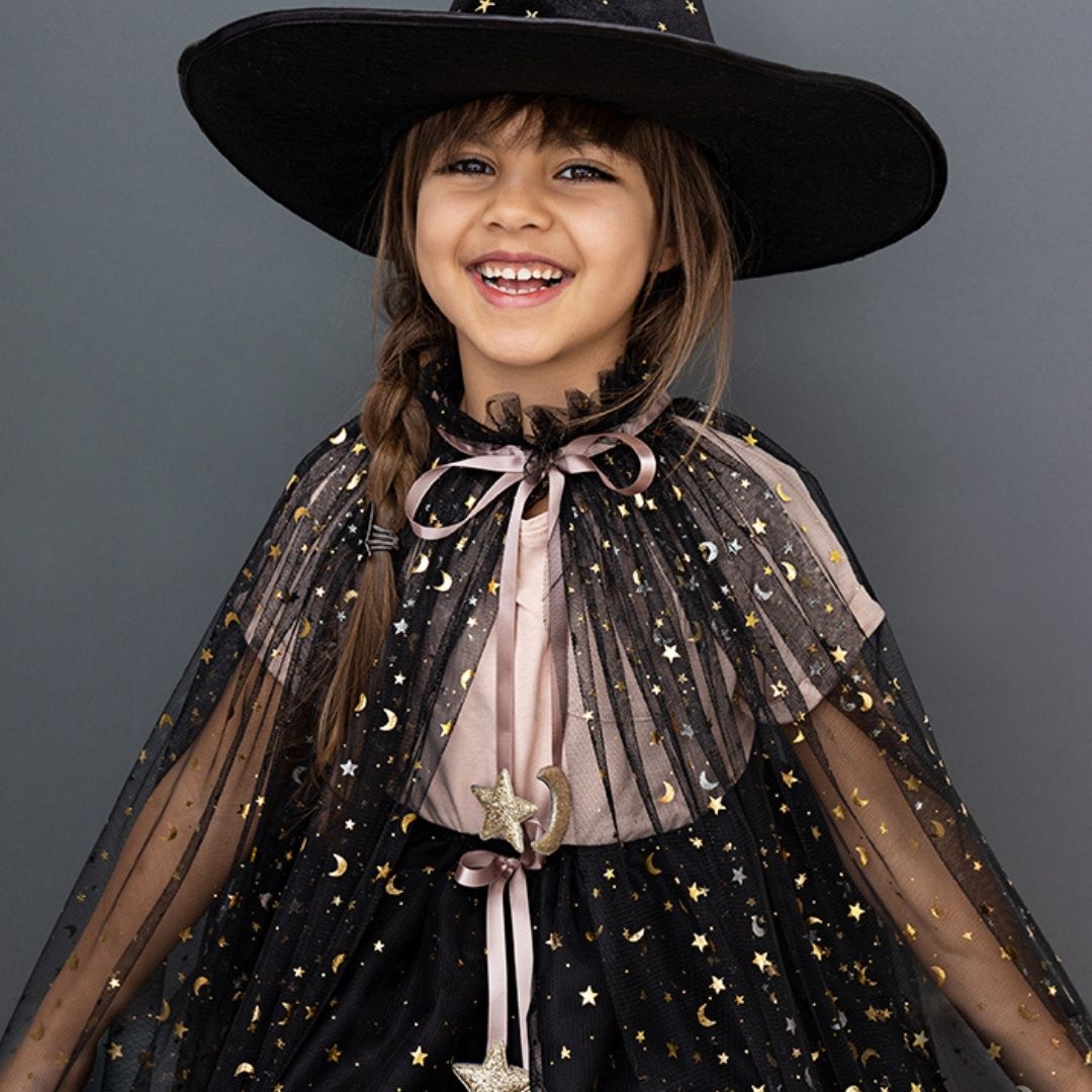 Pige med høj heksehat, tryllestav og lang sort kappe i tyl med rosa satinbindebånd, og små guldstjerner og måner, fra Mimi & Lula fås hos Nordic Simply