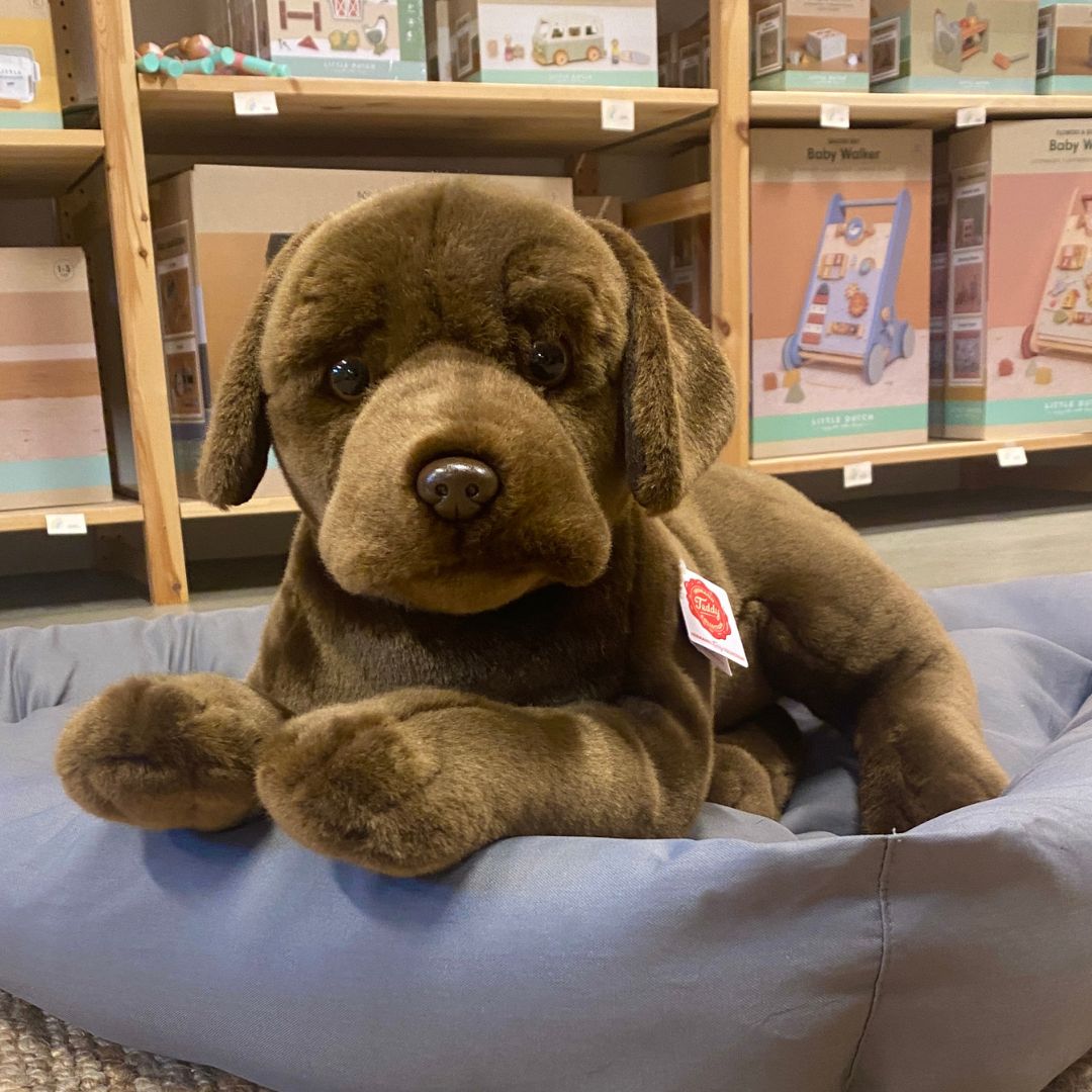 Stor brun labrador bamse, ligger i grå hundekurv, ligner ægte hund fra Teddy Hermann fås hos Nordic Simply