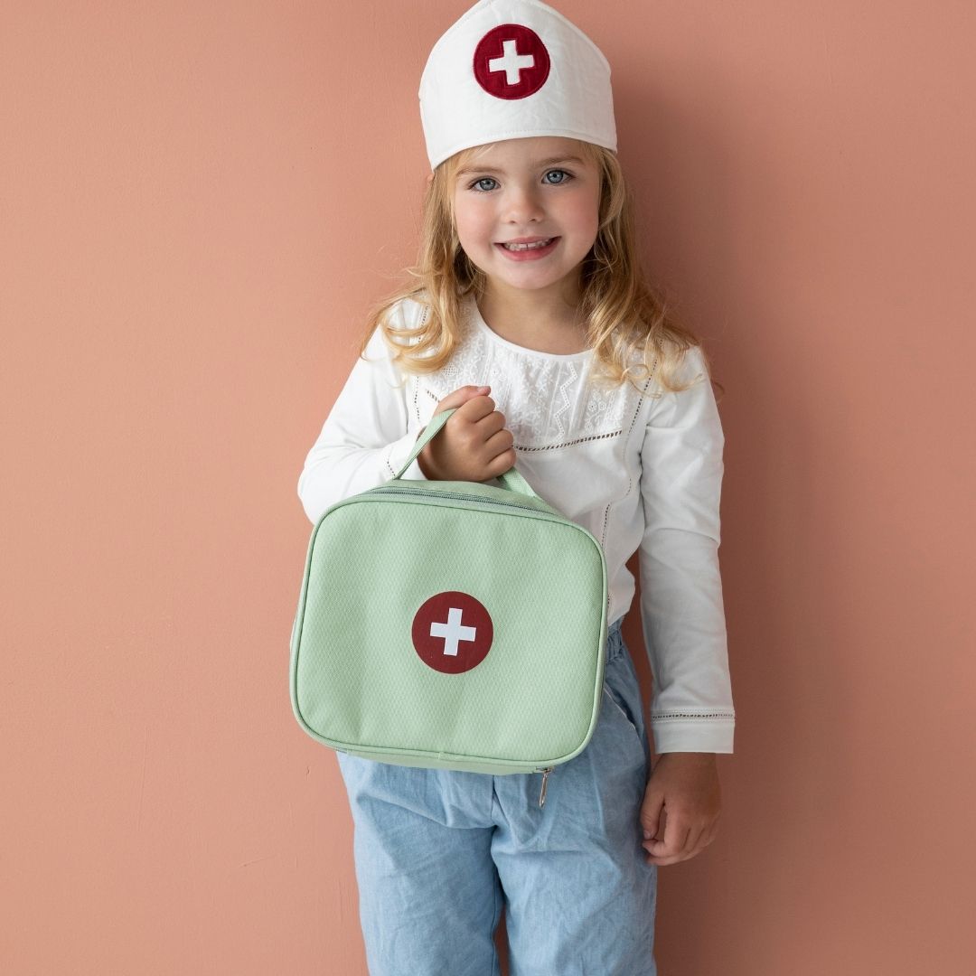 Pige med læge-hat står med grøn lægetaske fra Little Dutch på rosa baggrund, fås hos Nordic Simply