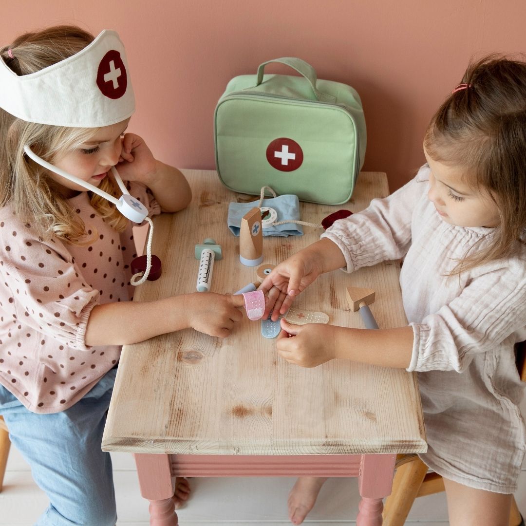 To piger ved bord leger læge, en pige har stetoskop om halsen, anden pige giver plaster på læge-legesæt i bedste kvalitet fra Little Dutch, fås hos Nordic Simply