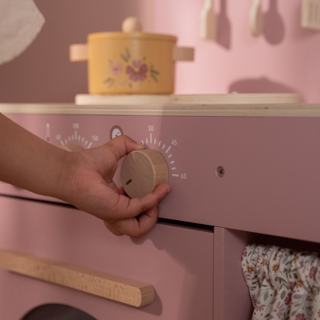 Legekøkken i rosa træ med tilbehør. Barn håndterer knopper til komfur og kogeplader på legekøkkenet