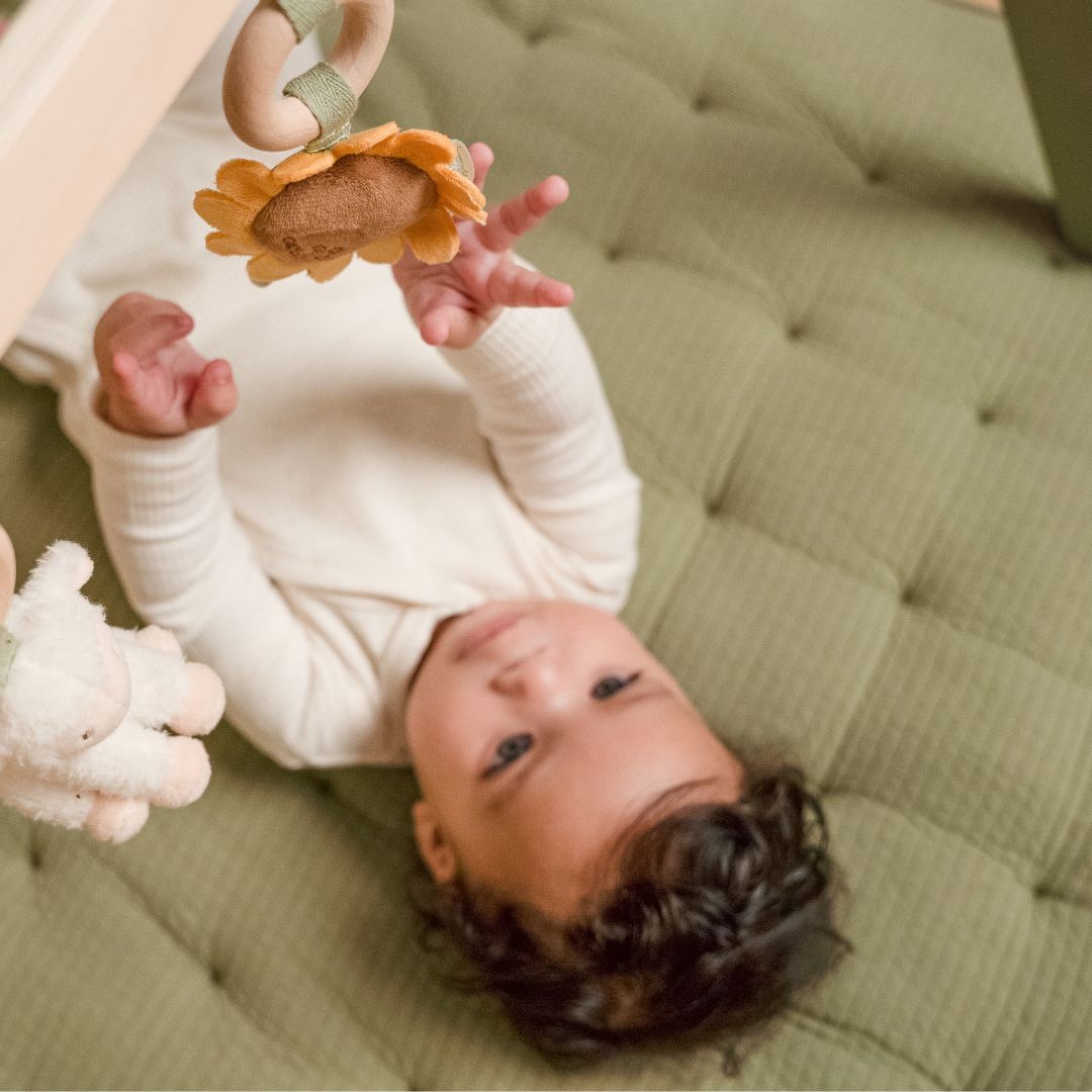 Baby ligger på oliven farvet legetæppe under aktivitetsstativ fra Little Dutch, fås hos Nordic Simply