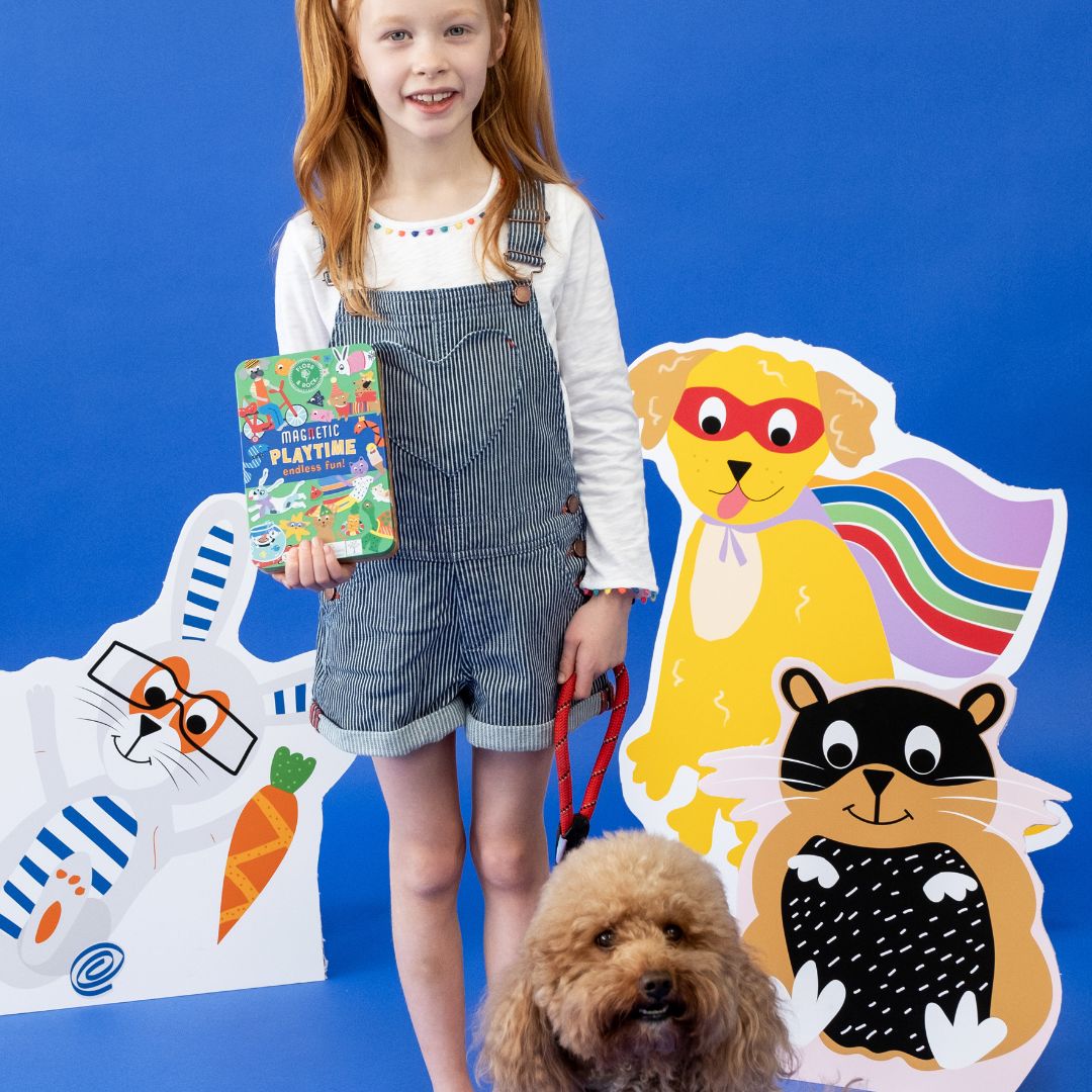 Pige holder magnetisk legesæt med kæledyr, set på blå baggrund med dyr i baggunden. Rejselegetøj til fordybelse, finmotorik på flyrejse og i bilferie, fås hos Nordic Simply