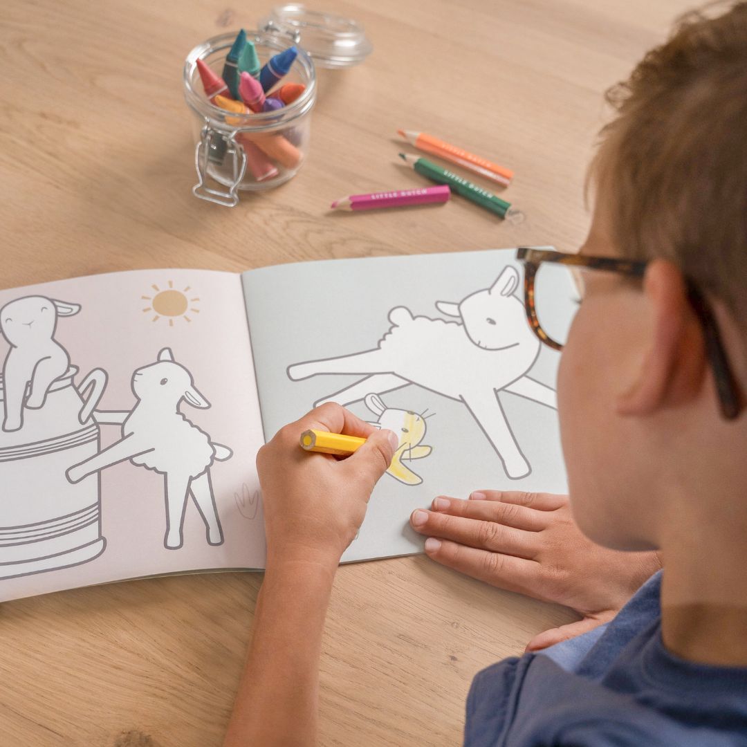 Barn, set over skulderen, tegner i malebog med motiver af bondegården fra Little Dutch. God fra 2 år og op