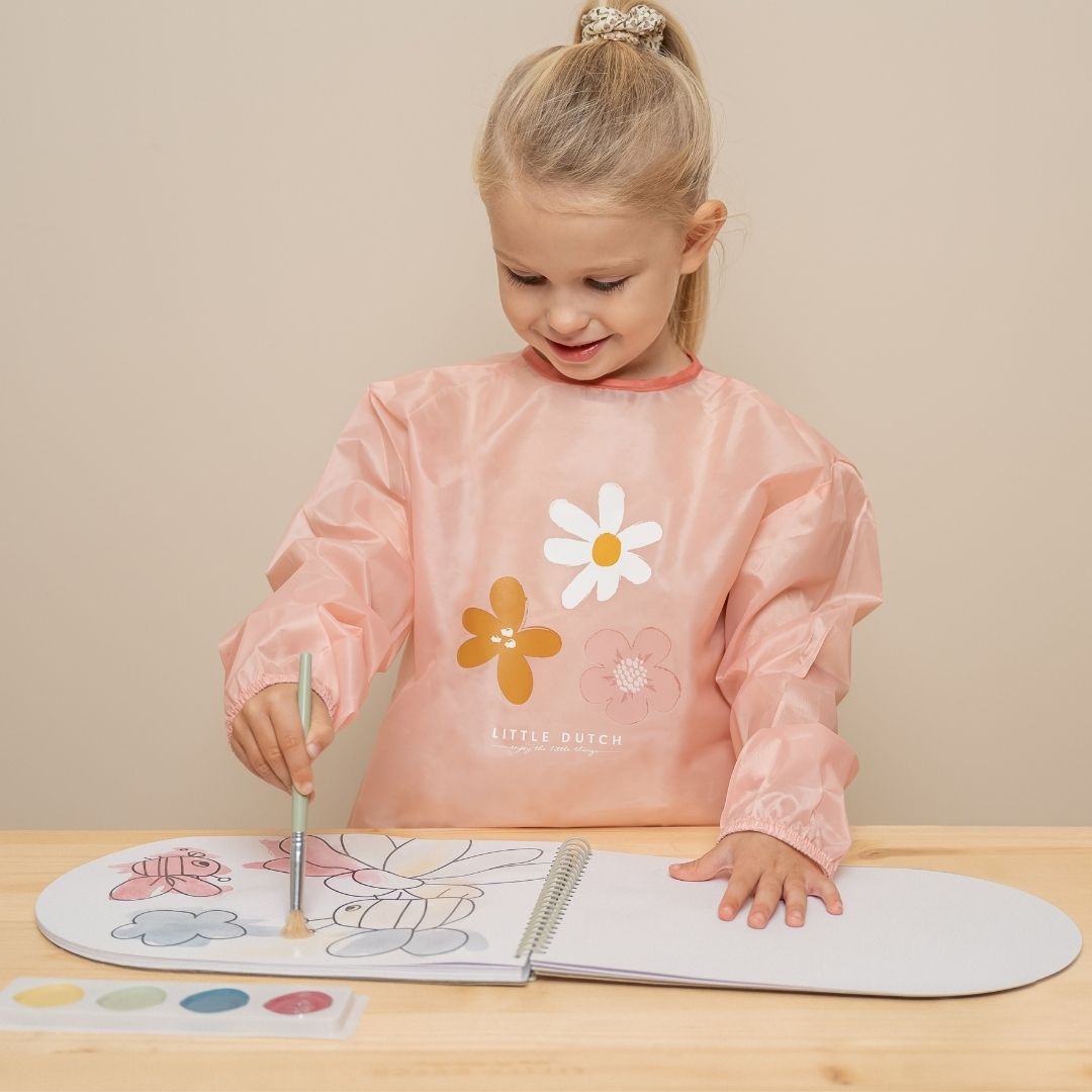Pige ned rosa forklæde maler bi og blomst med pensel i malebog, fra Little Dutch