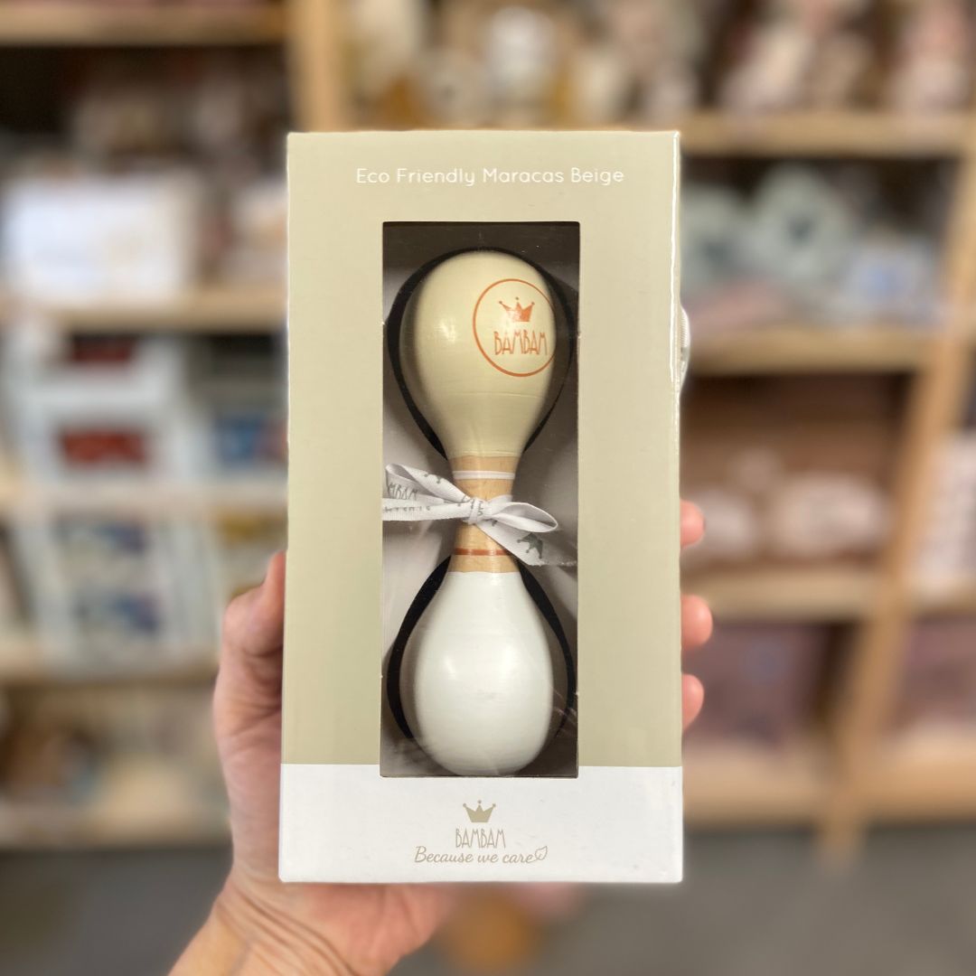 Hånd holder gaveæske med beige og hvid maracas i træ fra BamBam med rundt BamBam logo. Dejligt lille instrument til tumling 18 måneder og op, fås hos Nordic Simply.