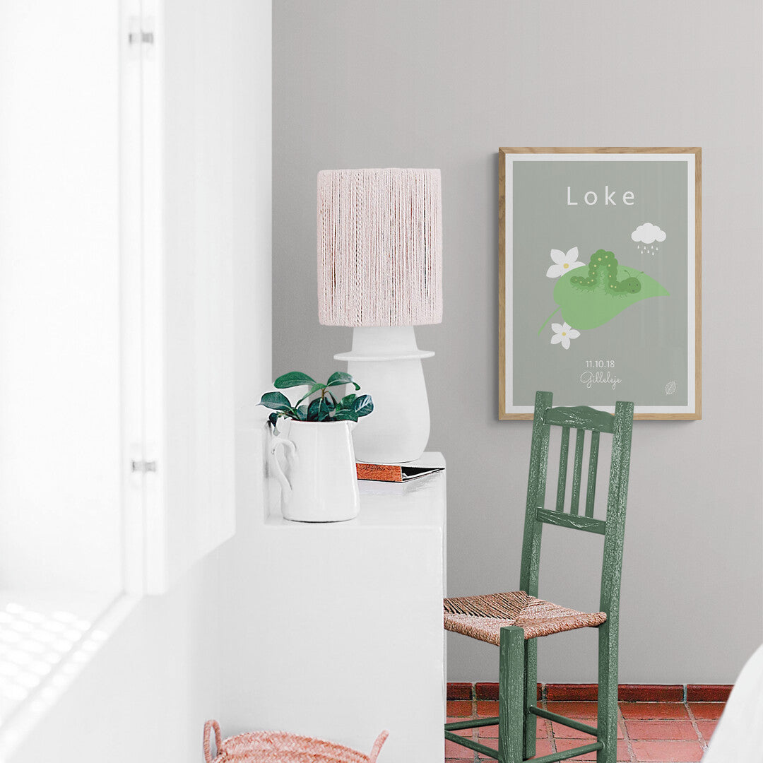 Grøn plakat med illustration af kålorm, personlig plakat til barn med navn, fødselsdato og by, set i træramme på lys væg i stue fra Nordic Simply