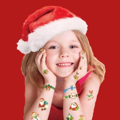 pige med nissehue på rød baggrund med jule-stickers på armene og neglestickers på neglene fra Avenir, fås hos Nordic