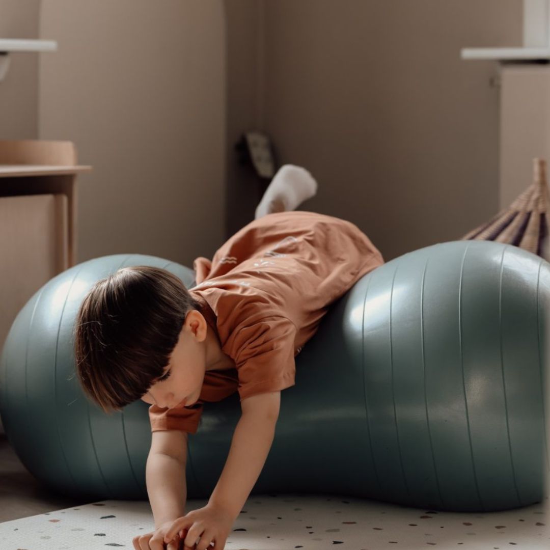 Barn tumler på blå peanutformet balancebold til sanseleg, motorisk udvikling og balance.