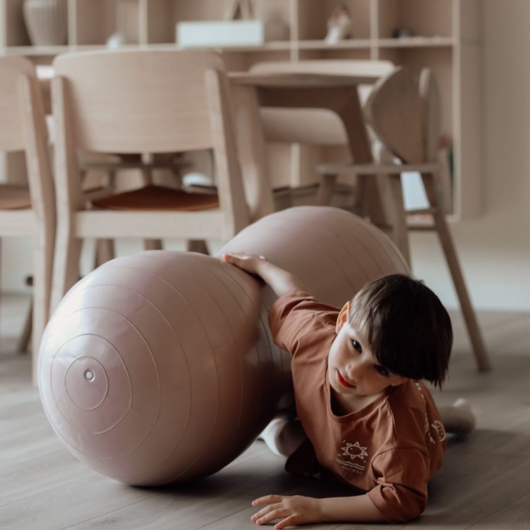 Barn tumler med rosa peanutformet balancebold til sanseleg, motorisk udvikling og balance.
