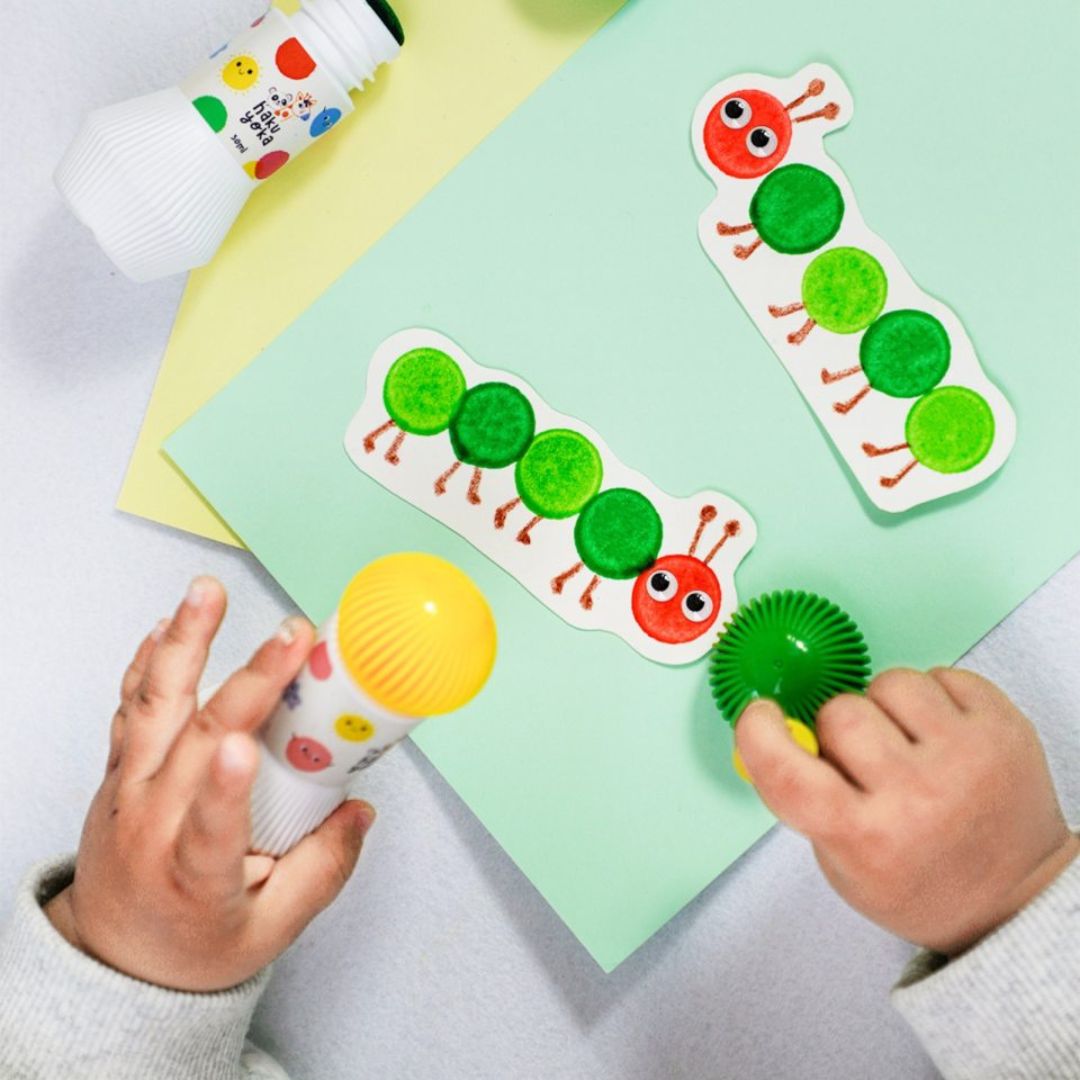 Barn bruger prikmarkør i klare farver til at skabe et farverigt kunstværker med en sød grøn larve.