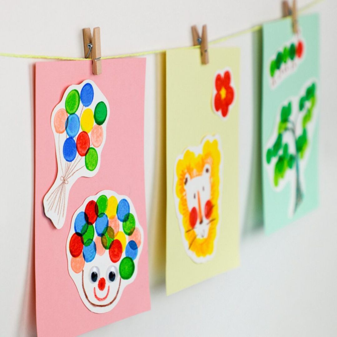 Farverige børnetegninger, lavet med prikmarkører i klare farver, hænger på snor med klips