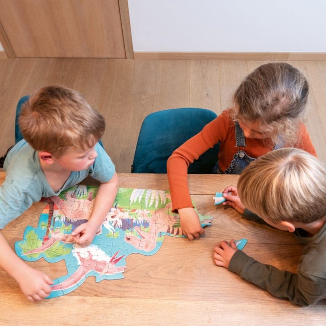Tre børn ved bord lægger puslespil med dinosaurer, 100 brikker fra Scratch fås hos Nordic Simply