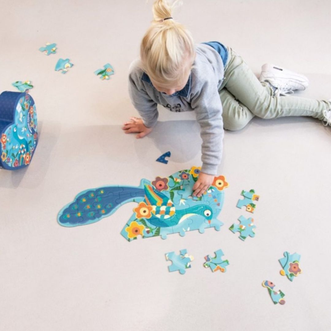 Barn sidder på lyst gulv og lægger puslespil med blå påfugl fra Scratch fås hos Nordic Simply