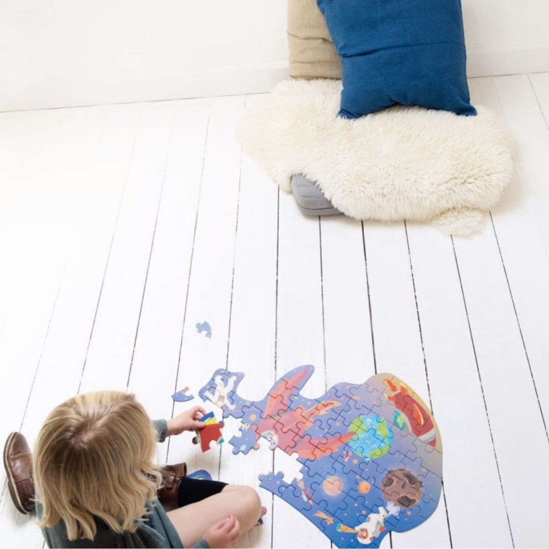 Barn på hvidmalet trægulv lægger puslespil med rød rumraket fås hos Nordic Simply