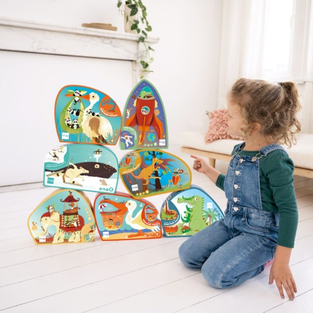 Barn sidder ved 7 puslespil stablet ovenpå hinanden, øverst til højre ses puslespil med rumraket fra Scratch fås hos Nordic Simply