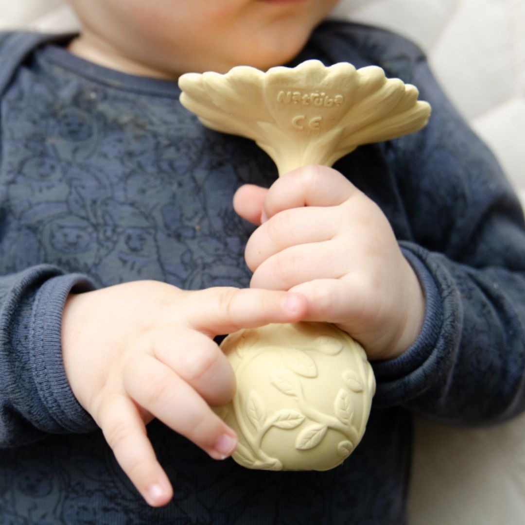 Hænder holder rangle formet som en gul marguerit, med teksturer, lavet i naturgummi af Natruba, fås hos Nordic Simply