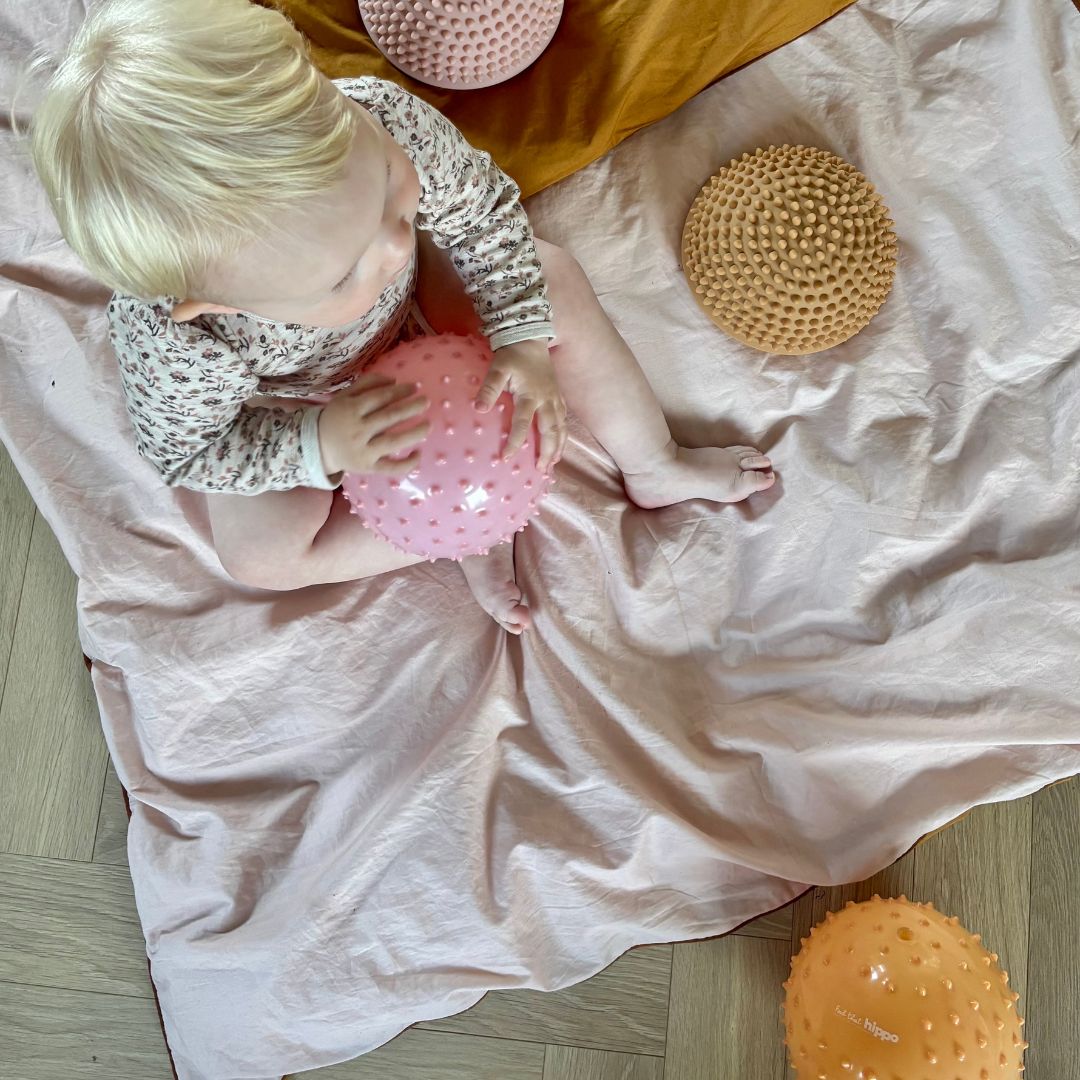 baby sidder på dyne med rosa og orange sansebolde fra Find that Hippo, på dynen ses også to lyse sansesten
