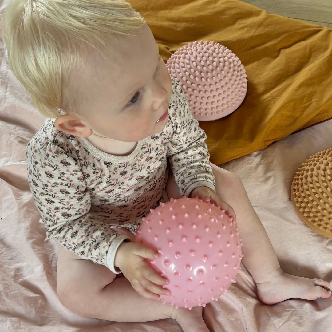 baby sidder i stue med rosa sansebold og lyse sansesten i baggrunden fra Find that Hippo