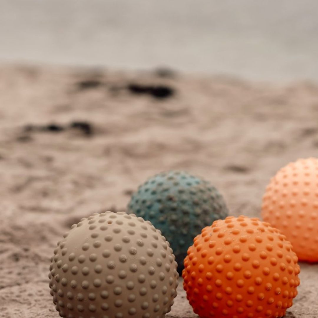 Fire store farverige sansebolde med nopret overflade, ligger på strand, ideelle til motorisk leg og sansestimulation.