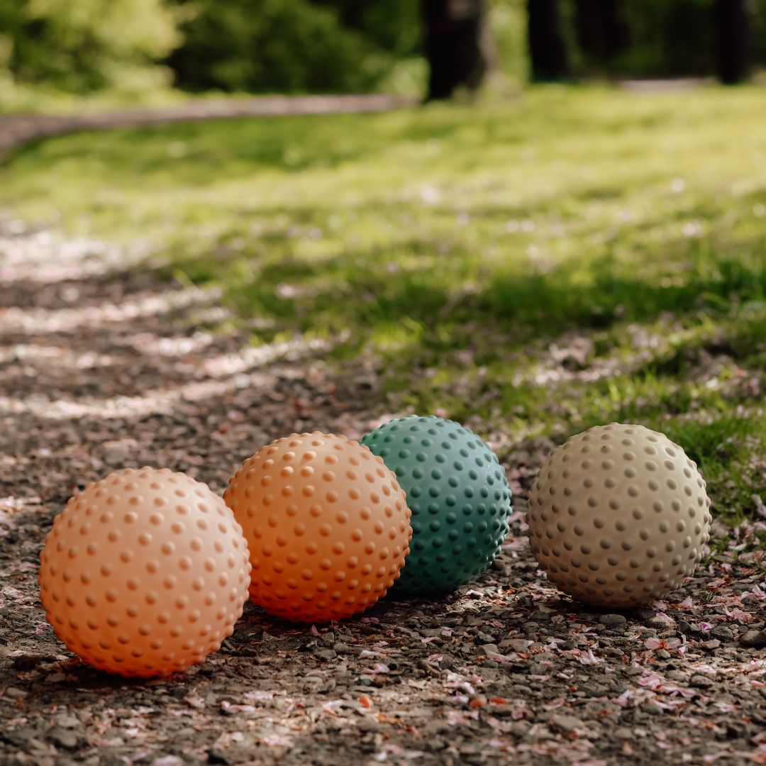 Farverige sansebolde i rosa, orange, blå og grøn ligger på sti i naturen, perfekte til motorisk leg og sansestimulation ude og inde.