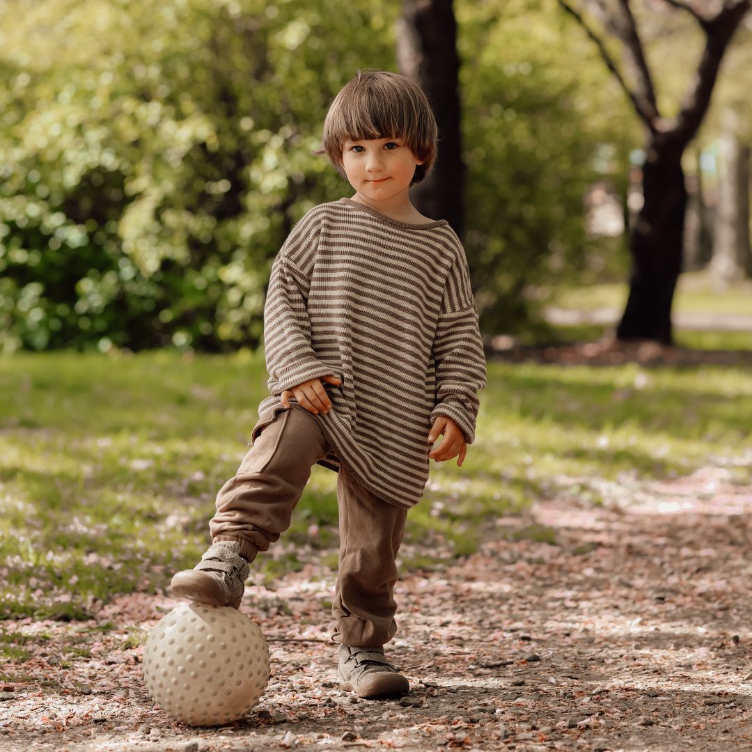 Barn står på sti med fod på grøn sansebold med knopper, perfekt til motorik og sansestimulation ude og inde.
